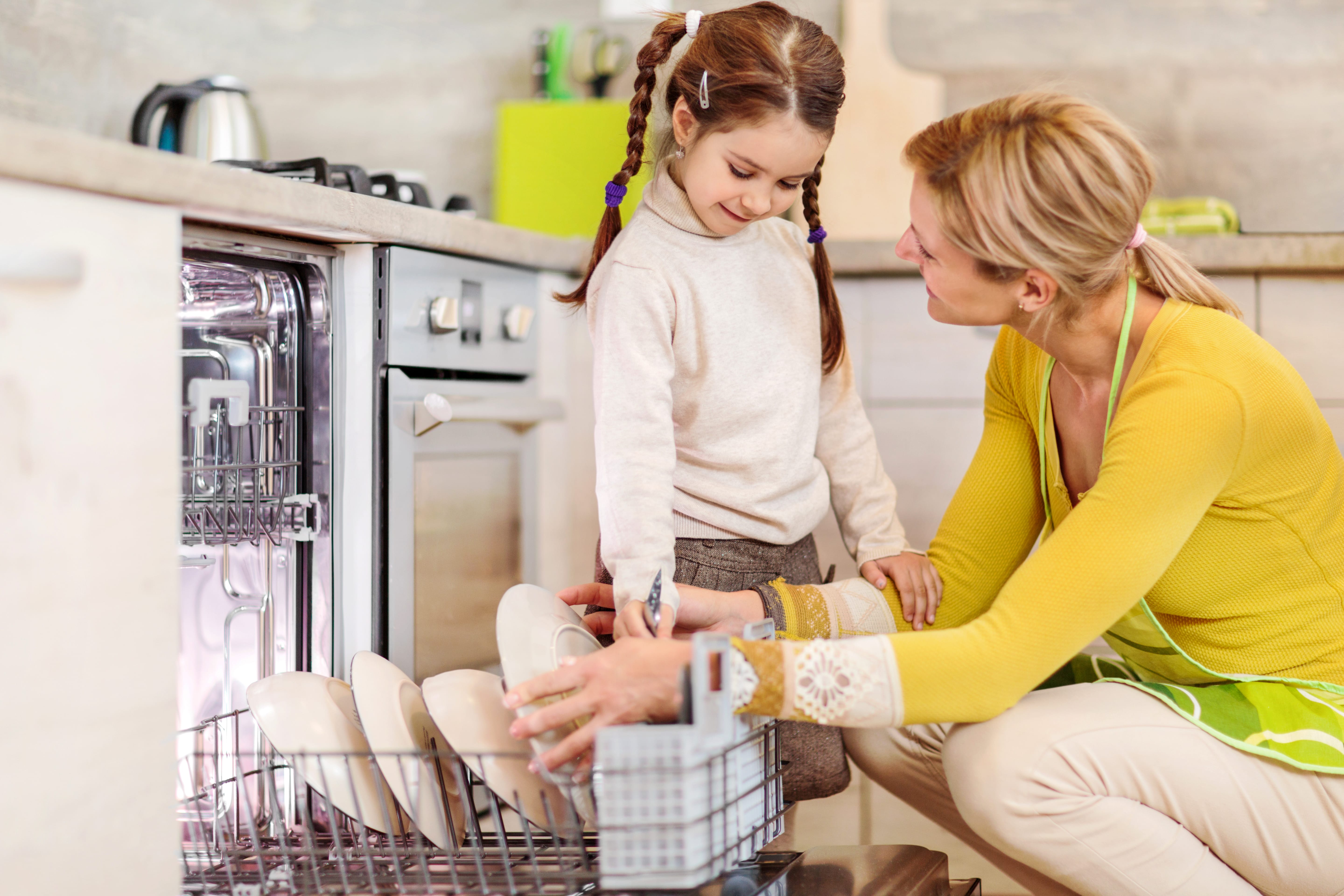 Adult and child in kitchen loading a dishwasher together