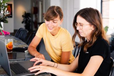Two adults sitting at a table looking at a laptop screen