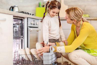 Adult and child in kitchen loading a dishwasher together