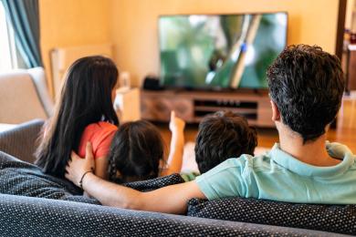 Two adults and children sitting and watching television