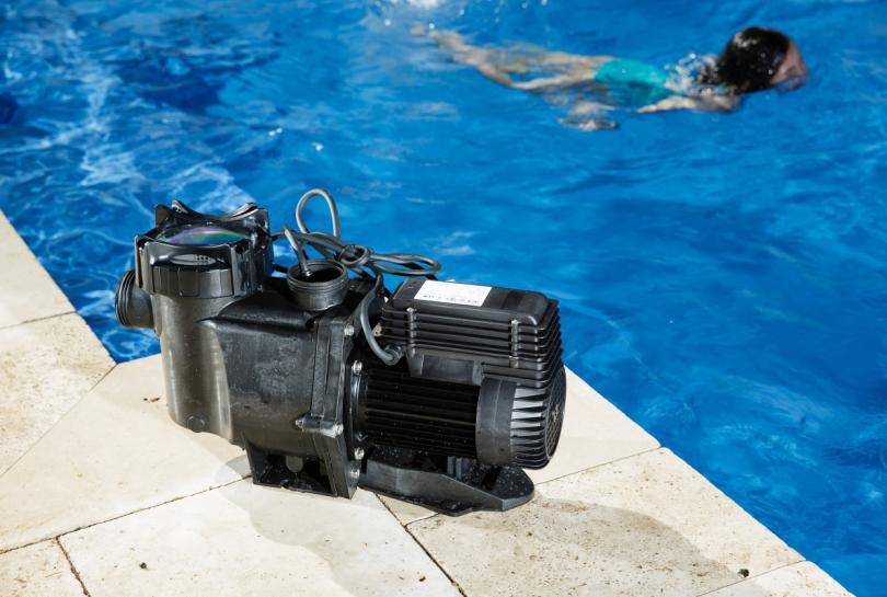 brand new swimming pool pump placed next to a bright clean pool